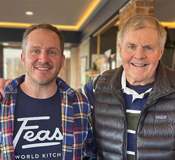 Группа из пяти человек стоит вместе в ярко освещенном коридоре больницы, улыбаясь в камеру. Двое носят стетоскопы и медицинскую одежду, один — толстовку Университета Гонзага, остальные одеты в повседневную или деловую одежду, представляя смесь студентов и медицинских работников.